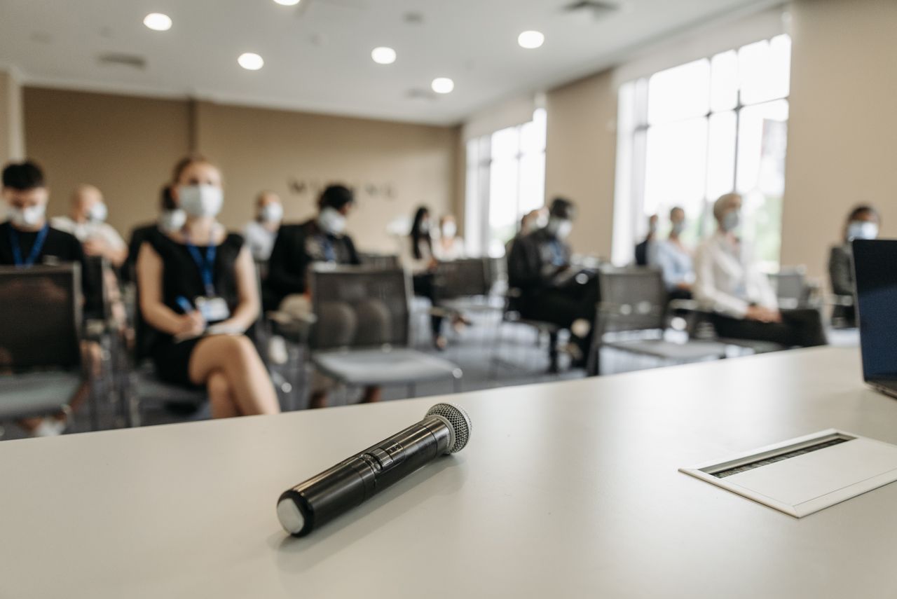 About A business conference room setting with masked participants and a microphone in the foreground.